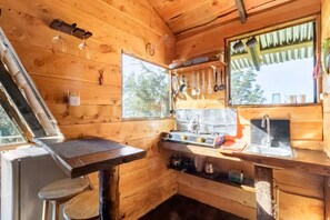 A compact wooden cabin with a kitchenette, a window, and a small stool.