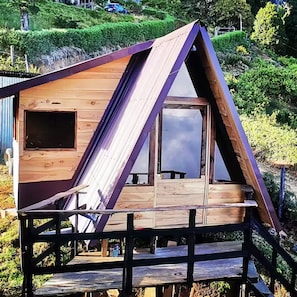 A wooden cabin with a triangular roof, a small deck, and a window.