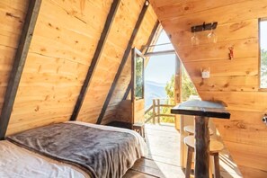 A wooden interior with a bed, a table, and a view of the outdoors.