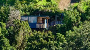 Une cabane entourée d’une forêt dense, dotée d’une terrasse en bois et d’un petit porche.