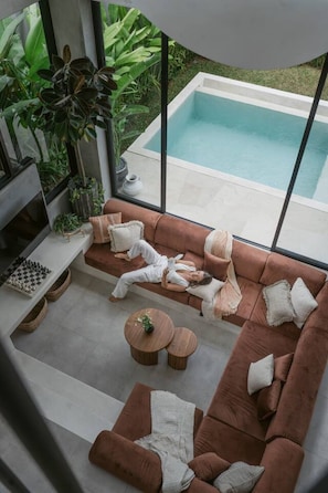 Ein modernes Wohnzimmer mit Blick auf einen Pool, ausgestattet mit einer Couch, einem Couchtisch und einem Schachbrett.