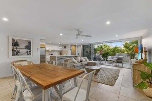 A modern living space with a dining area, kitchen, and a large sliding glass door leading to a balcony with plants. - 3 Sundeck Gardens 72 Alexandra Parade (Maroochydore)