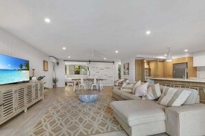 A modern living room with a flat-screen TV, a sofa, a dining area, and a kitchen. - 3 Sundeck Gardens 72 Alexandra Parade (Maroochydore)