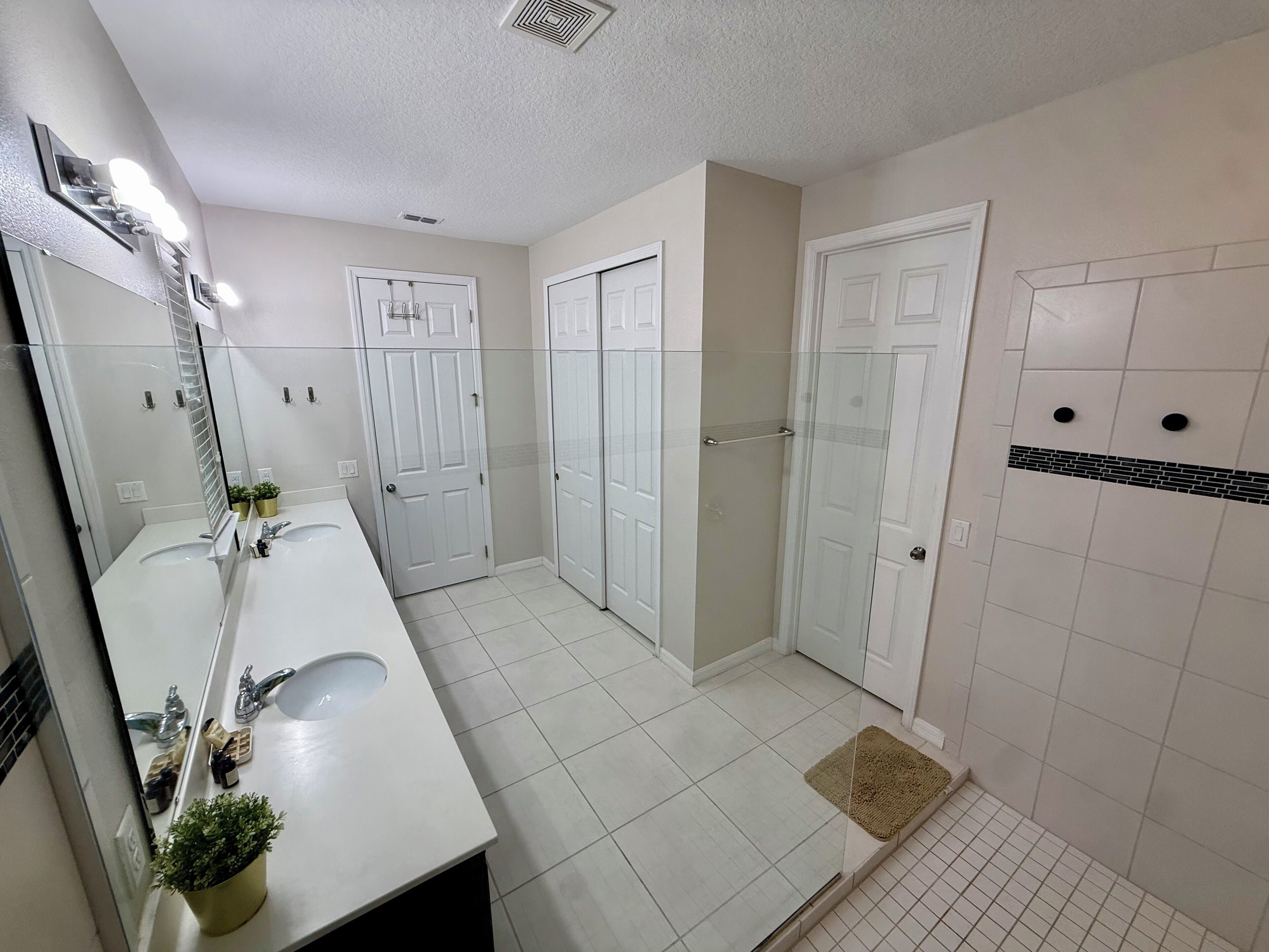 A modern bathroom with two sinks, a large mirror, a shower, and a glass-enclosed door.