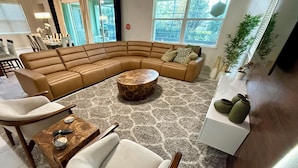 Un salon moderne avec un canapé d’angle aux lignes courbes, une table basse ronde, un fauteuil blanc et un buffet agrémenté de vases décoratifs.