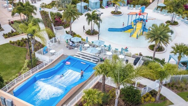 Un espace piscine doté d’un toboggan, de chaises longues et de palmiers.