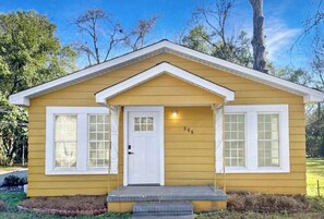 A yellow single-story house with a white door and two windows, number 306, with a small porch and steps leading up to the entrance.