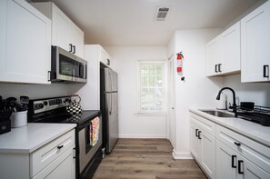 A kitchen with white cabinets, a stainless steel refrigerator, a microwave, and a black stove.