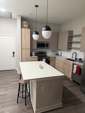 Una cocina moderna con una isla central, electrodomésticos de acero inoxidable e iluminación colgante.