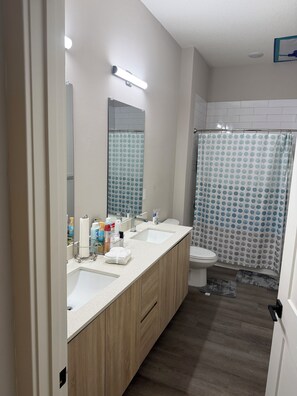 Un baño con dos lavamanos, un inodoro, una cortina de ducha y un espejo.