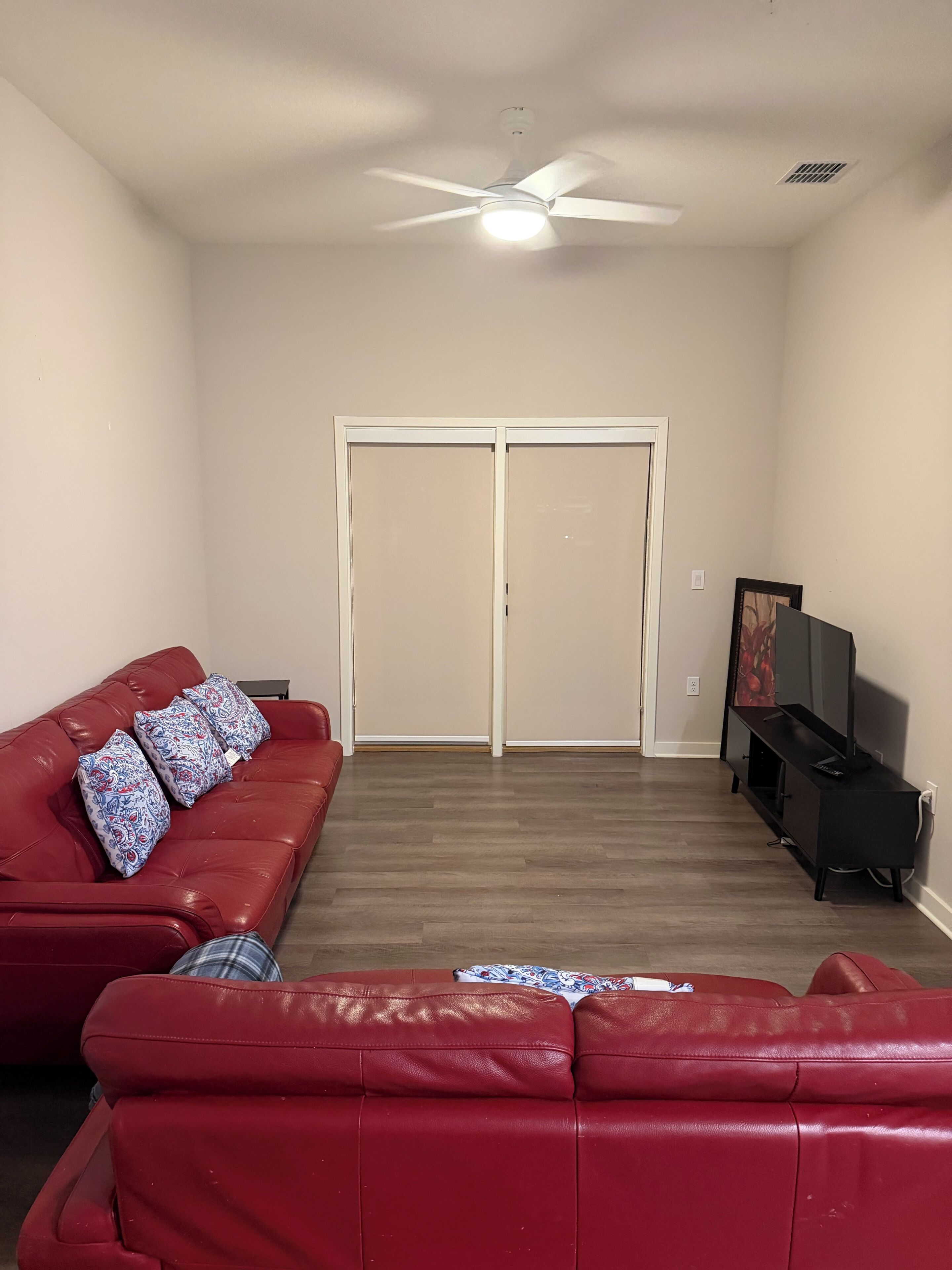 A living room with a red leather couch, a ceiling fan, a television, and a sliding door.