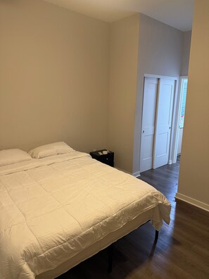 Un dormitorio con una cama grande, una mesita de noche y una puerta que da a otra habitación.