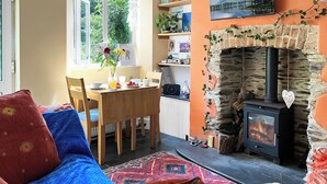 Ein gemütliches Wohnzimmer mit Kamin, einem Essbereich mit Tisch und Stühlen sowie Blick ins Grüne durch ein Fenster.