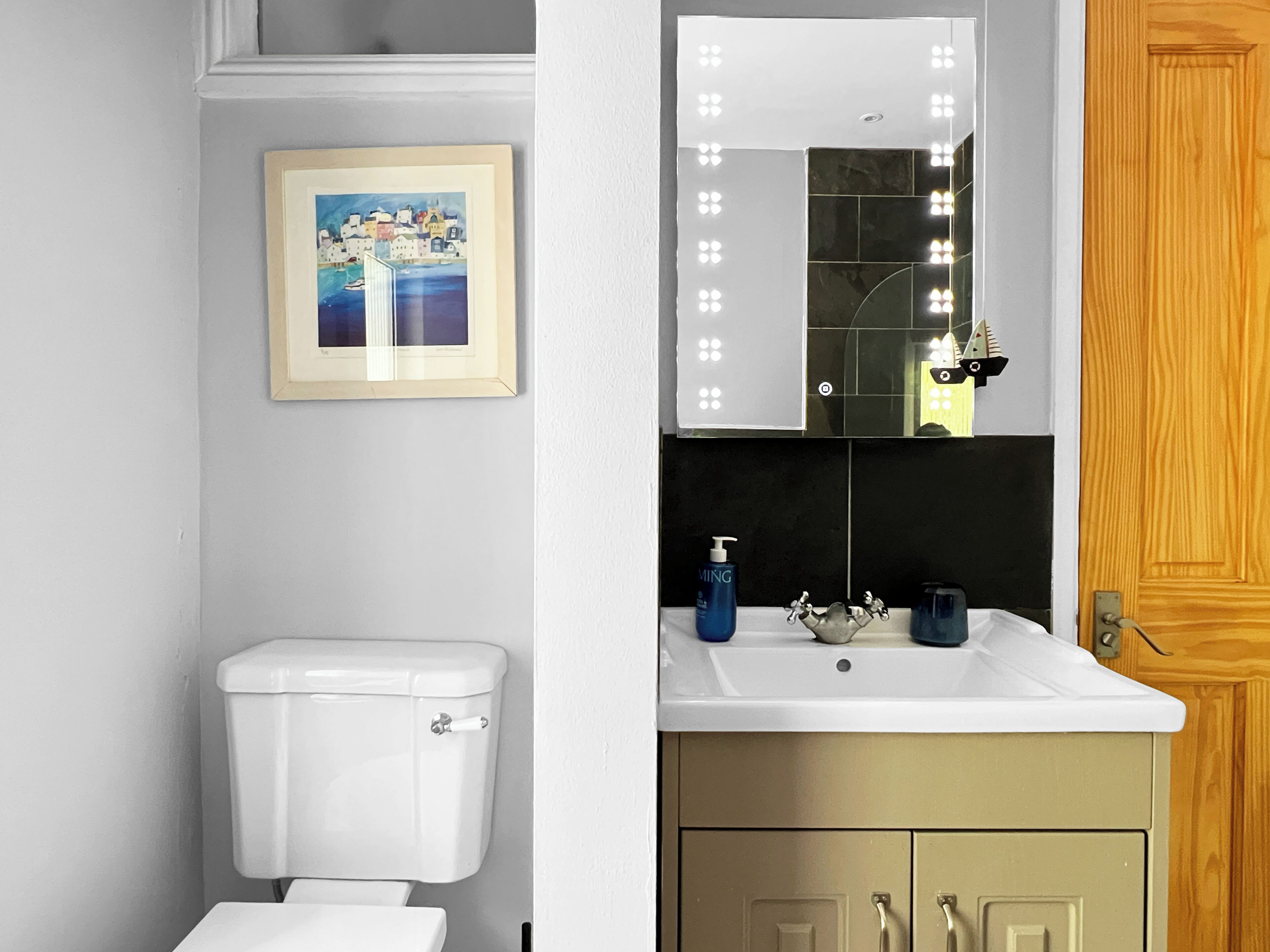 Ein Badezimmer mit Toilette, einem Waschbecken mit Spiegel und einem gerahmten Bild an der Wand.