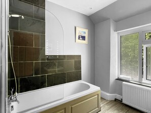 Une salle de bain avec une baignoire, une douche et une fenêtre avec des stores.