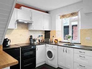 Une cuisine équipée d’une cuisinière, d’un four, d’un lave-linge et d’une fenêtre donnant sur l’extérieur.