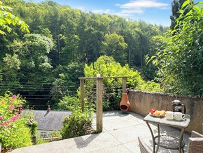 En terrasse med et bord, stole, en terracotta krukke og en pergola i træ.