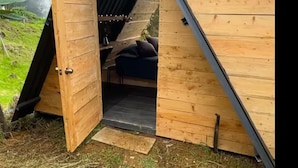 A wooden structure with a slanted roof, a door, and a small seating area inside.