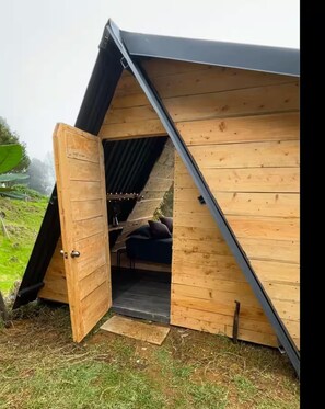 A wooden structure with a slanted roof, a door, and a small seating area inside.