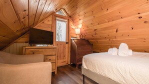 A cozy attic bedroom with a wooden ceiling, a TV on a dresser, a lamp, and neatly made towels on the bed. - Cottage AND Tiny House on Lake Pontoon Available (Lake Lure)