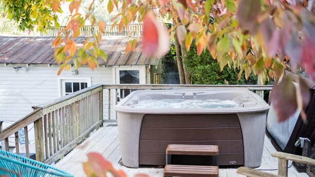 A hot tub on a wooden deck with a wooden railing and a chair. - Cottage AND Tiny House on Lake Pontoon Available (Lake Lure)