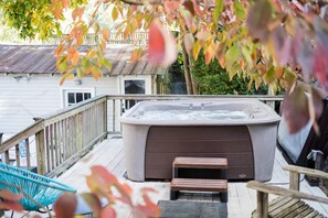 Un jacuzzi en una terraza de madera con barandilla de madera y una silla.