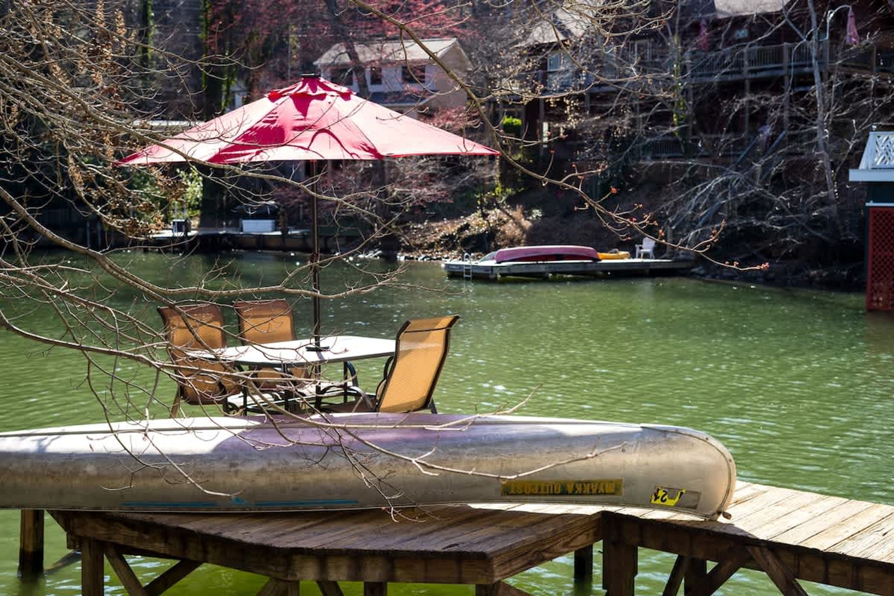 A wooden dock with a metal boat, a table with chairs, and a red umbrella.