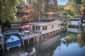 Uma casa flutuante atracada em um cais, com um deque, um barco pequeno e uma canoa também atracada.