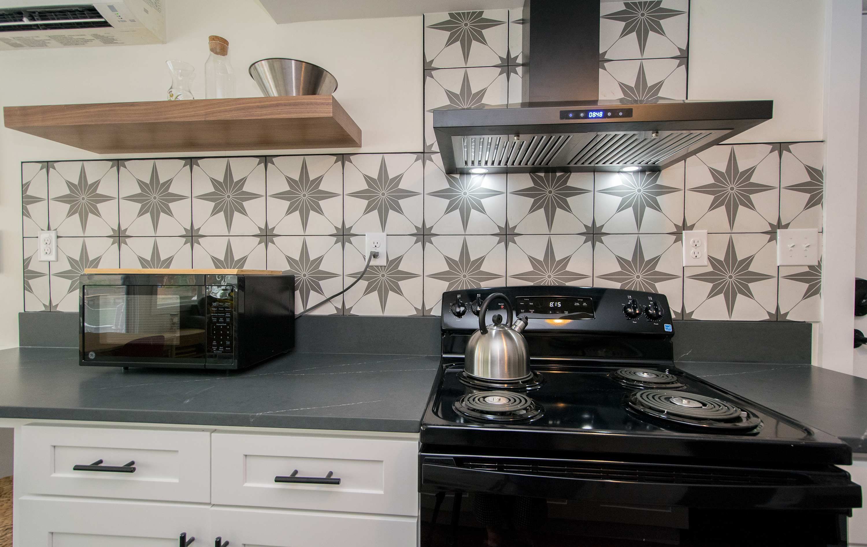 A kitchen with a microwave, stove, and decorative tiles.