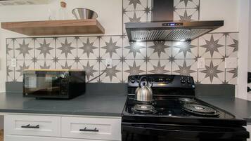 A kitchen with a microwave, stove, and decorative tiles.