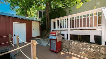 A deck with a barbecue grill, a wooden fence, and a building with a door.