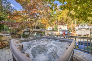Uma banheira de hidromassagem rodeada por folhagem outonal, um deck de madeira e vista para uma casa e um píer.