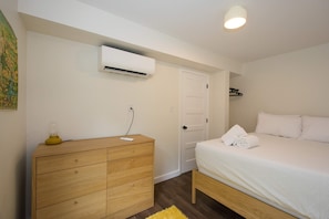 A bedroom with a bed, a wooden dresser, an air conditioning unit, and a door. - Dog Friendly Cottage on Lake Pontoon Available (Lake Lure)