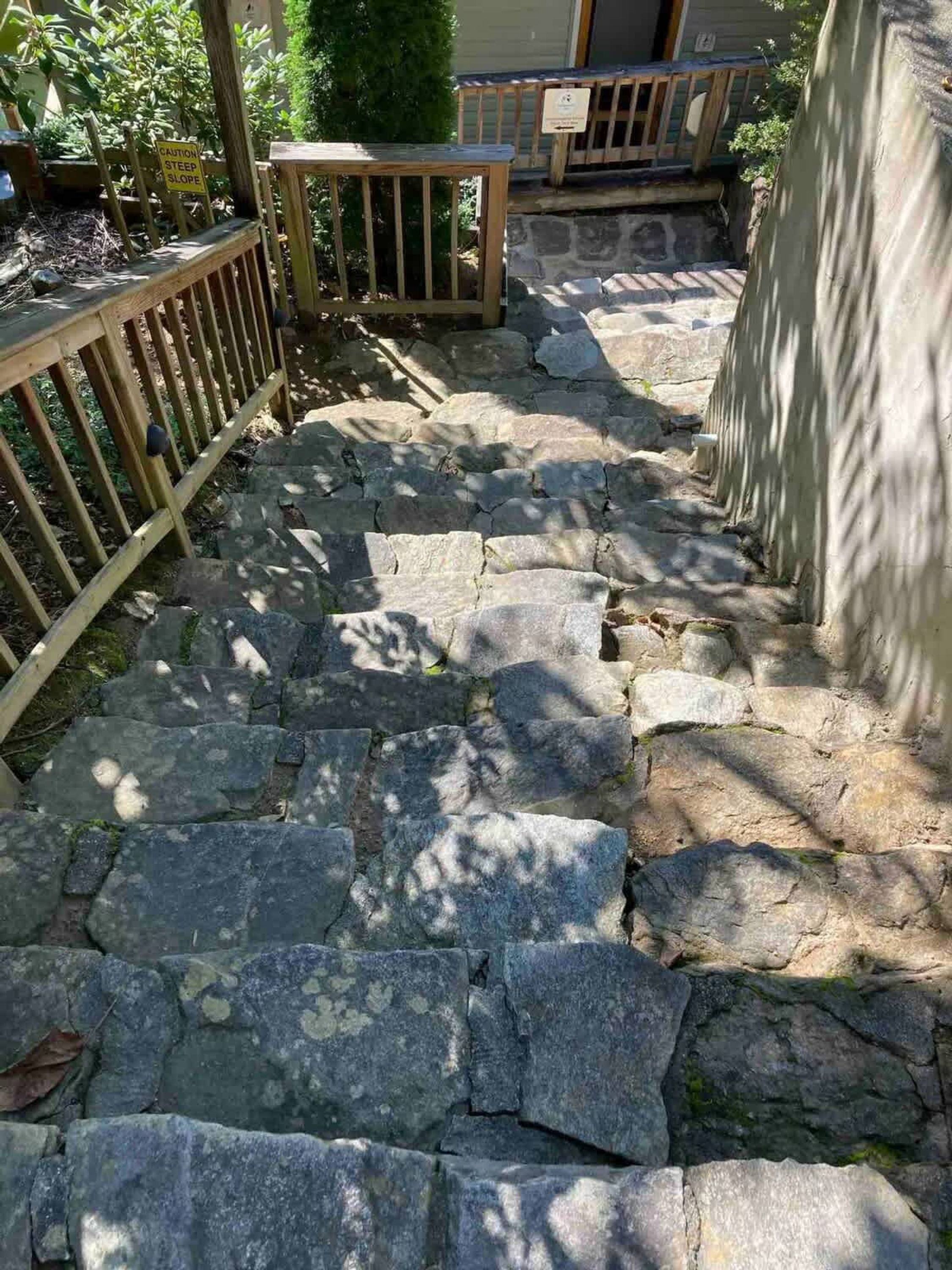 A stone staircase leading up to a wooden deck with a caution sign for a steep slope.