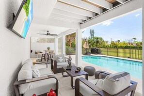 Ein überdachter Außenbereich mit Pool, Sitzgelegenheiten und einem an der Wand befestigten Fernseher.
