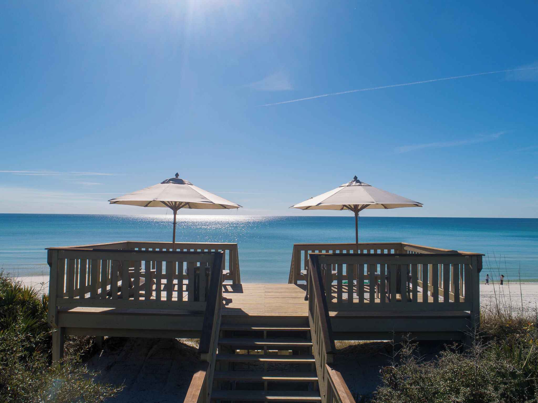 Una terrazza in legno con due sedie da spiaggia e ombrelloni che si affaccia su una spiaggia.