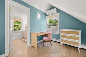 Una habitación con un escritorio de madera, una silla rosa, un aparador blanco y una ventana con vistas a la vegetación.