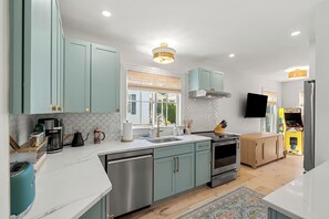 Een moderne keuken met turquoise kastjes, roestvrijstalen apparatuur, een raam met zonwering en een kleurrijk vloerkleed.