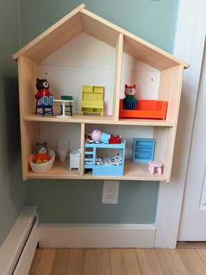 Een poppenhuis met twee verdiepingen, een tafeltje, een stoel, een plankje en een raam.