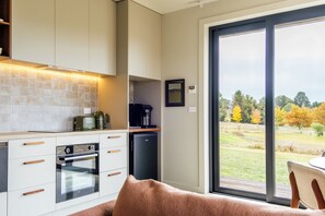 A modern kitchen with a built-in oven, a coffee maker, and a view of a garden through a sliding door.