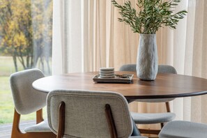 A round dining table with a vase of greenery, a tray with plates, and chairs.