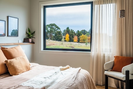 A bedroom with a large window, a bed, a chair, and a shelf with a plant.. Fiora Estate: Luxury Accomodation in Laggan Village NSW