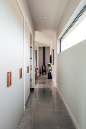 A hallway with white walls, a polished floor, and a large window on the right.