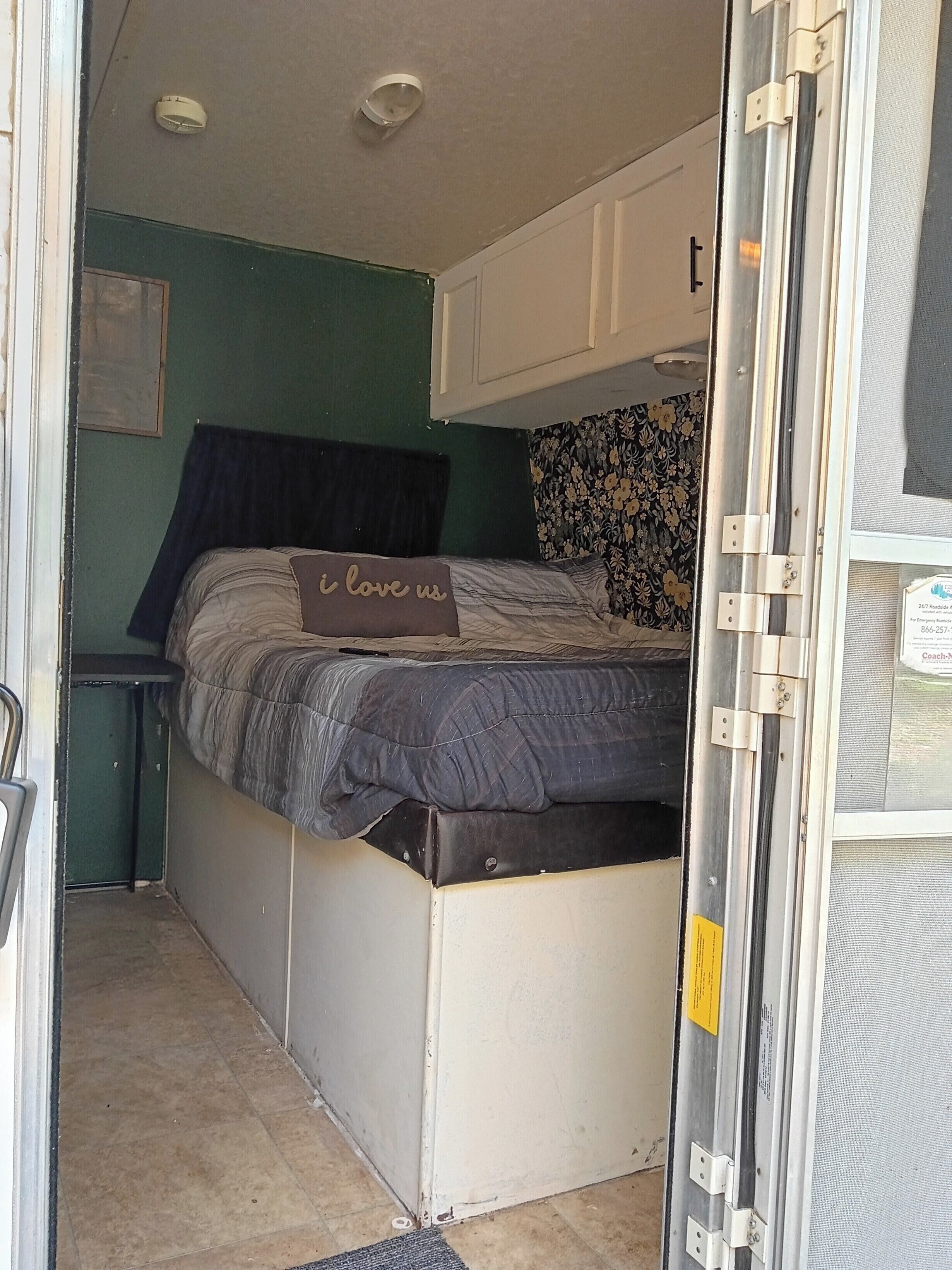 A compact RV interior with a bed, a small table, and a door leading to the outside.