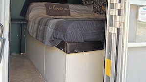 Een compact interieur van een camper met een bed, een klein tafeltje en een deur naar buiten.