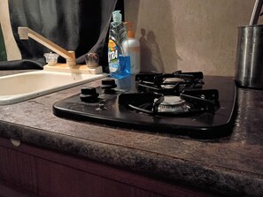 Una cocina con estufa a gas, un lavamanos y una botella de detergente.