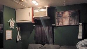 Een kamer met een bank, een airconditioningapparaat, een ingelijst schilderij en een bord aan de muur.