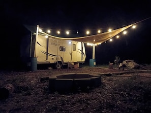 A caravan with a covered outdoor area, a small table, and a fire pit. - THE PAISLEY HIDEOUT 
Budget + 420 RV Stay 
 springs, parks, & Daytona close (Paisley)