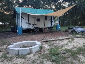 A mobile home with a covered porch and a fire pit in the foreground. - THE PAISLEY HIDEOUT 
Budget + 420 RV Stay 
 springs, parks, & Daytona close (Paisley)