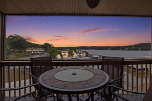 Ein Balkon mit rundem Tisch und Stühlen, mit Blick auf einen See, im Hintergrund Häuser.